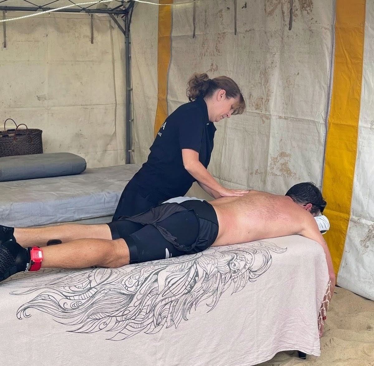 Caroline masse le dos d’un triathlète sous une tente, au bord de la plage